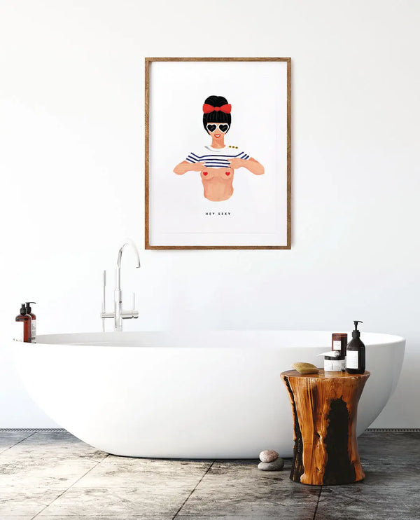 Modern wall art titled Hey Sexy featuring a pin-up girl in a striped shirt, framed above a white bathtub in a bright minimalist bathroom.