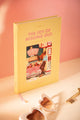 Jomo A5 hardcover notebook standing at an angle, showing the yellow cover, illustrated gas station scene and pink ribbon bookmark