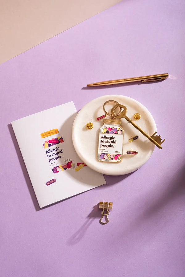 Allergic to stupid people Keychain - Top view on a purple background with a gold pen and paper clip.