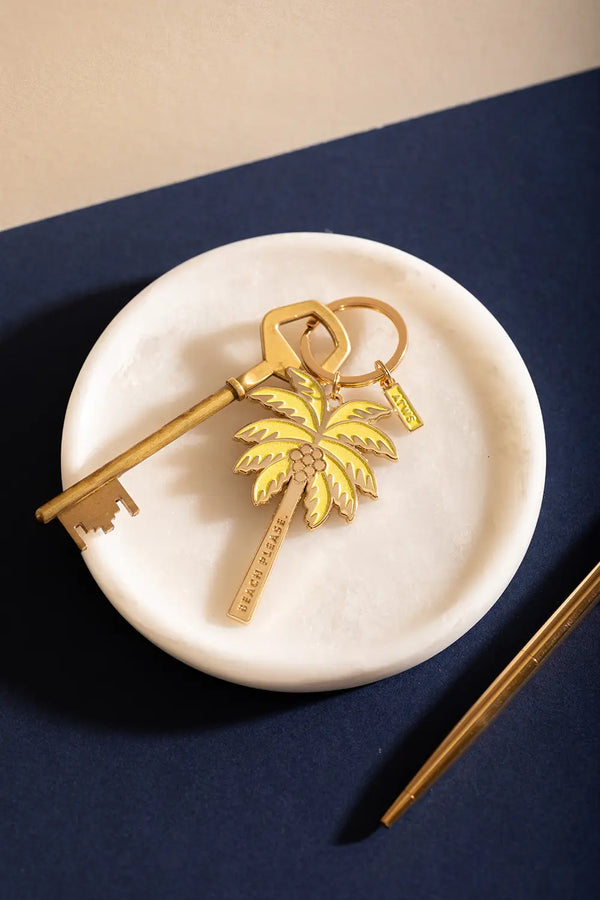 Beach please Keychain - Top view of the yellow and gold palm tree design on a white marble background.
