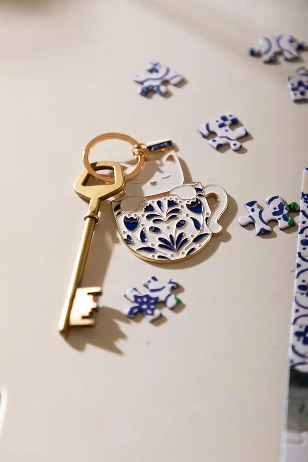 Cat in a mug Keychain - Lifestyle view on a white desk with blue and white puzzle pieces.