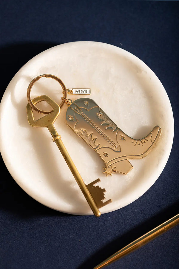 Cowboy Boot Keychain - Top view showing the detailed golden western boot design on marble.