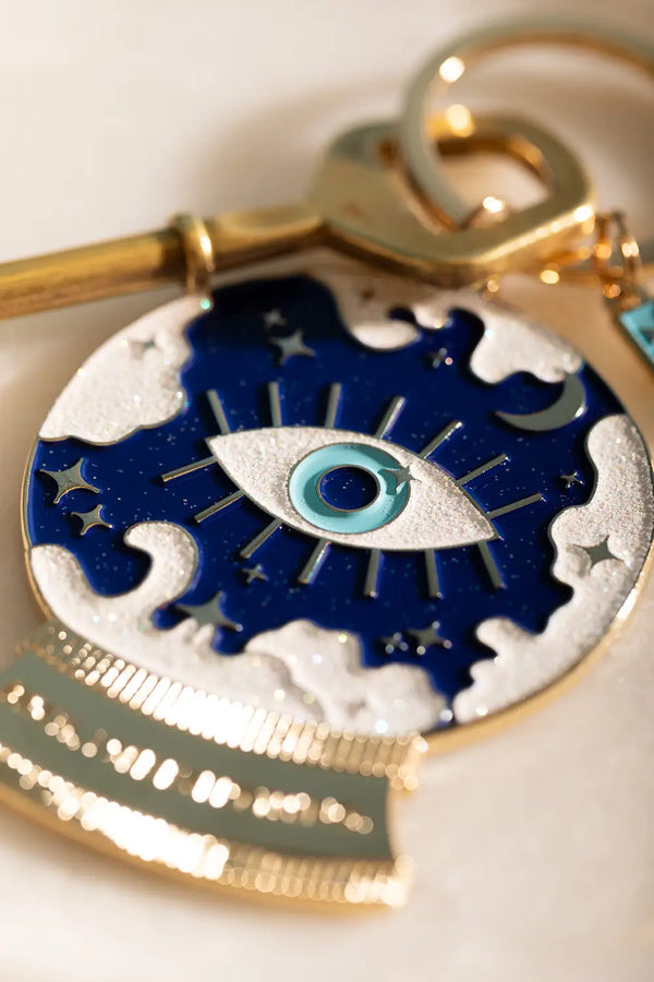I see everything Keychain - Close-up of the blue enamel eye and celestial glitter patterns.