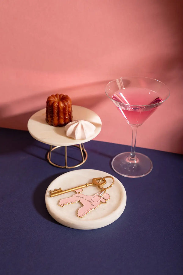 Poodle mood Keychain - Lifestyle view on a marble tray with a pink cocktail and pastries.