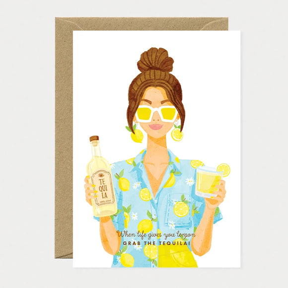 Illustrated greeting card of a woman wearing a lemon-print shirt and yellow sunglasses, with lemon slice earrings, holding a bottle of tequila and a glass of tequila with a lemon slice, text reading "When life gives you lemon, grab the tequila!"