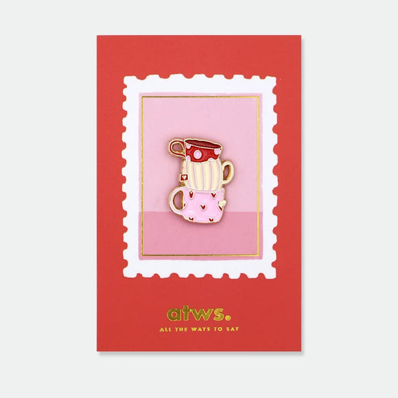 Enamel pin of three stacked teacups in red polka dot, cream stripe, and pink heart patterns