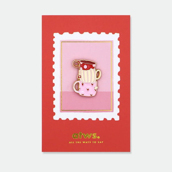 Enamel pin of three stacked teacups in red polka dot, cream stripe, and pink heart patterns
