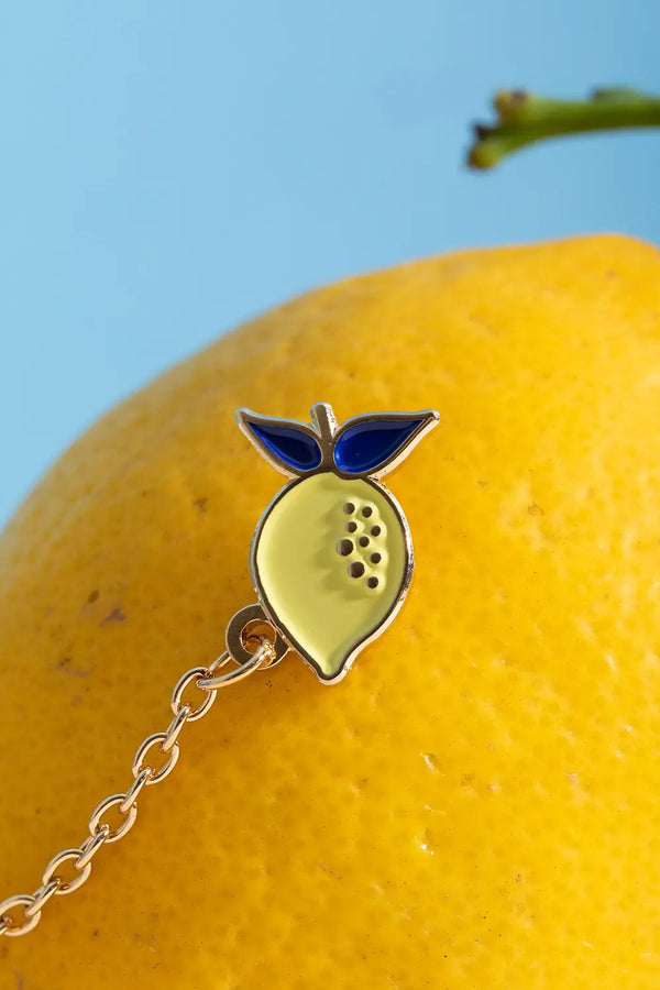 Duo Margarita Chain - Pins: close-up of the yellow enamel lemon pin with blue leaves on a real lemon.
