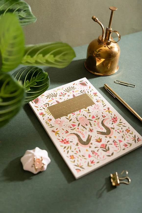 Pink Croco Notebook A5 - Lifestyle view on a dark green desk with a gold water sprayer and pen.