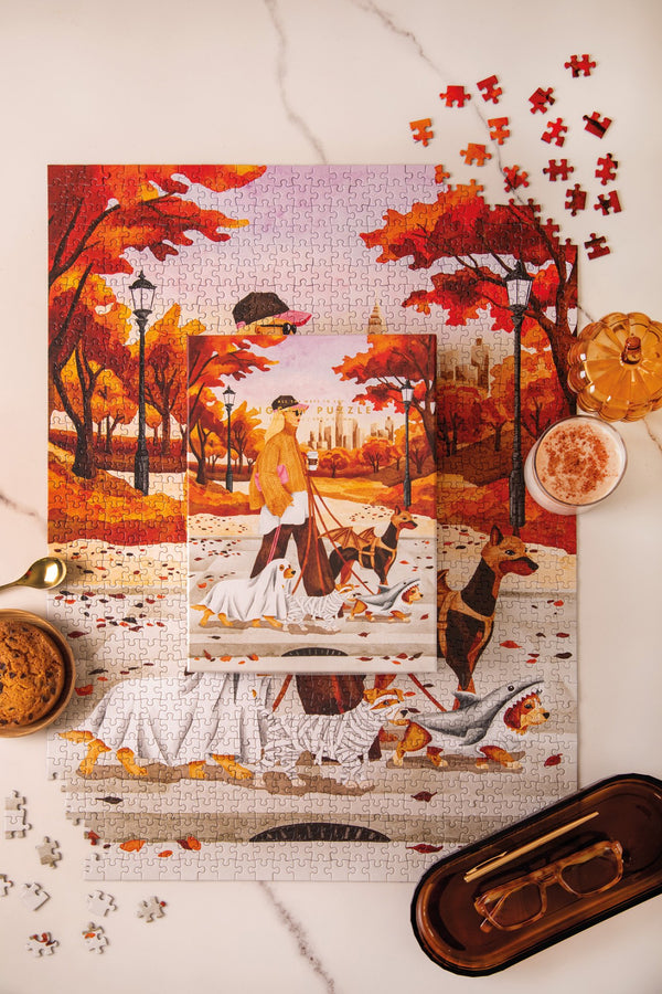 October Walks 1000 piece jigsaw puzzle and box, a woman walking dogs in Halloween costumes through an autumn park in New York
