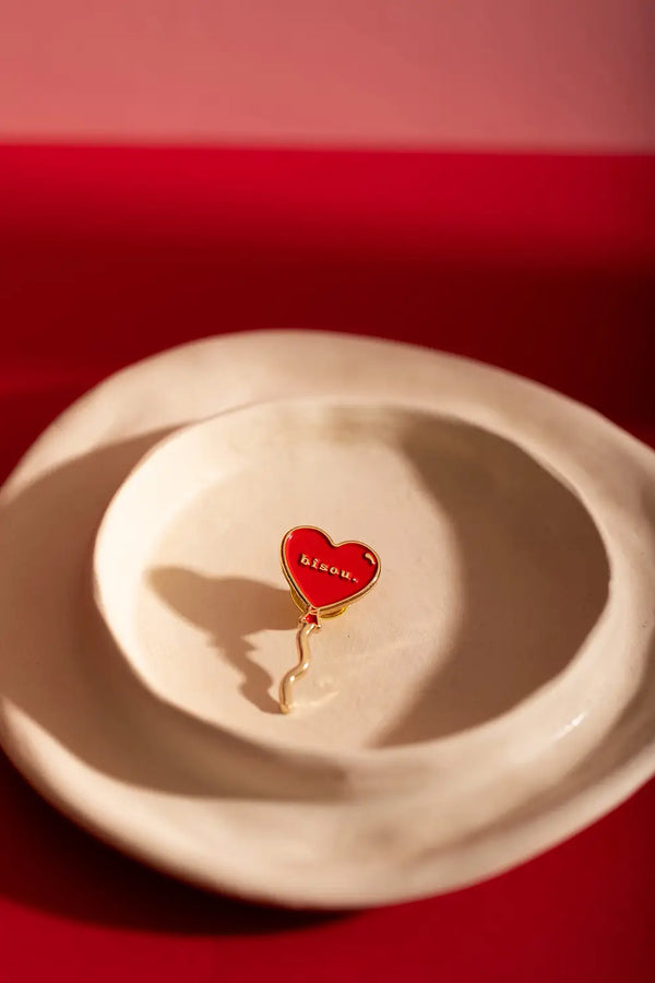 Bisou Enamel Pin - Red heart balloon pin centered on a white minimalist ceramic dish.