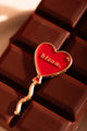 Bisou Enamel Pin - Detailed view of the red pin placed on a dark chocolate bar.
