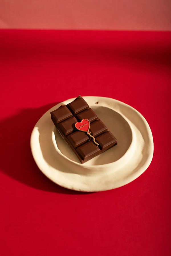 Bisou Enamel Pin - Lifestyle flatlay of the pin on chocolate and a white plate on red background.