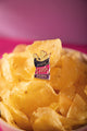 Potato chip bag enamel pin in navy, pink and purple with gold chips, resting on a bowl of crisps