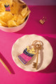 Potato chip bag enamel pin on a bowl of crisps, next to the matching "You are the crunchiest potato chip in the bag" keychain