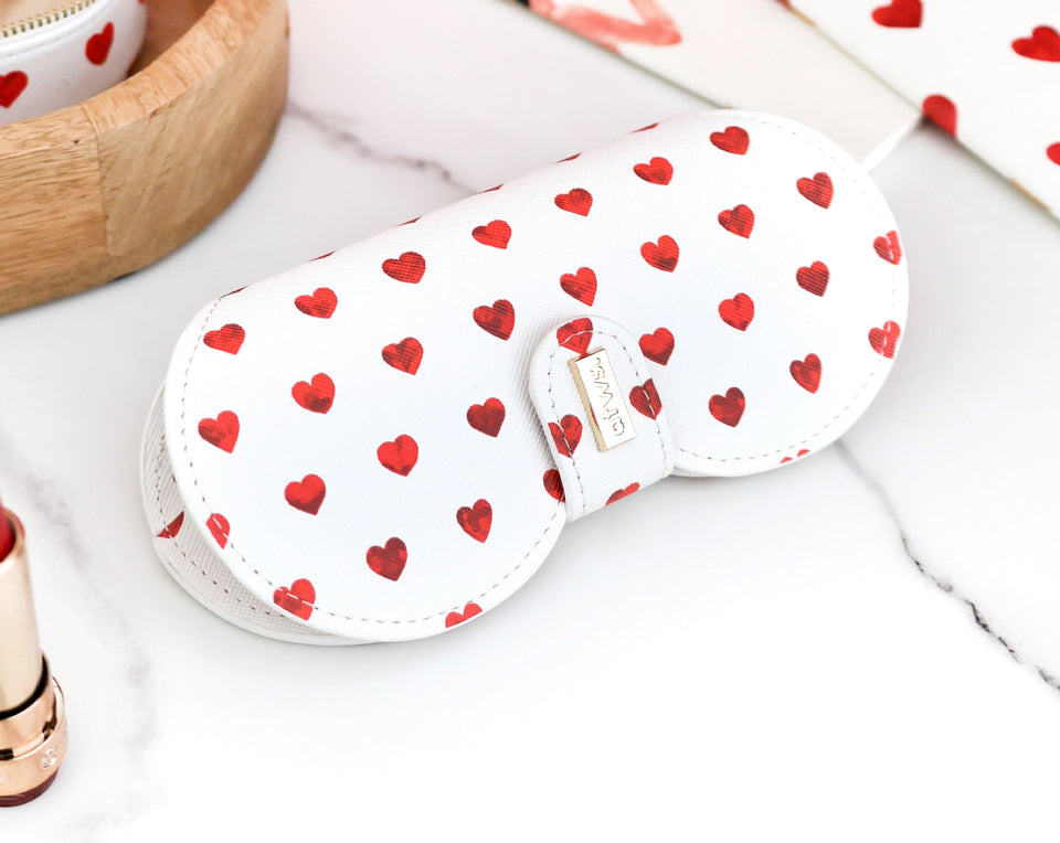 Elegant white eyeglasses case adorned with a delicate red heart pattern and a gold branded clip, placed on a chic marble surface.