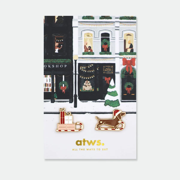 Set of two enamel pins: a sleigh loaded with wrapped presents, and a dachshund wearing a Santa hat riding a candy cane sleigh