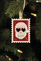 "It's Christmas B*tches" enamel Christmas ornament shaped like a postage stamp, Santa in heart sunglasses, hanging on a lit tree