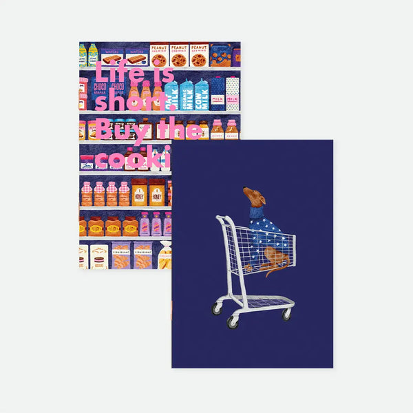 Sugar Market A6 pocket notebook duo covers by All The Ways To Say, one dark navy notebook packed with illustrated grocery shelves and "Life is short. Buy the cookies." text in pink lettering, the other featuring a dachshund in a sweater riding in a shopping cart on a navy background