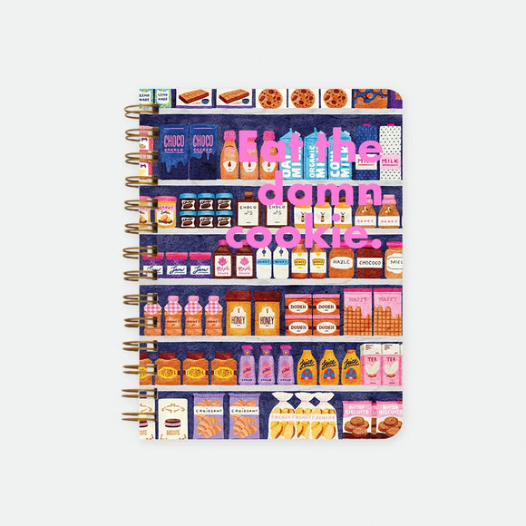 Sugar Market A5 spiral notebook by All The Ways To Say, illustrated grocery shelves packed with jams, milk and biscuits with "Eat the damn cookie." text in pink lettering across the middle, spiral binding visible on the left edge