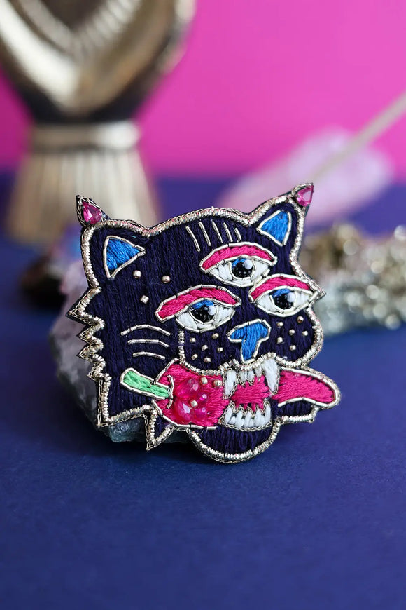 Close-up of a surrealist three-eyed tiger brooch highlighting the intricate silk shading, pink sequins, and gold metallic embroidery.