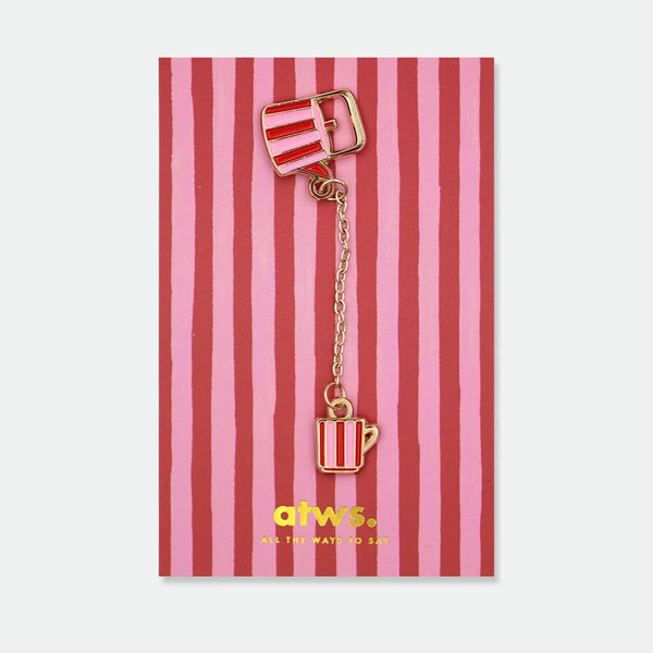 Enamel pin of a red and pink striped teapot connected by a gold chain to a matching striped teacup