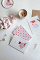 Together Cats collection – pink and white notebooks with red hearts and cat illustration, styled with marshmallows, coffee and stationery clips.